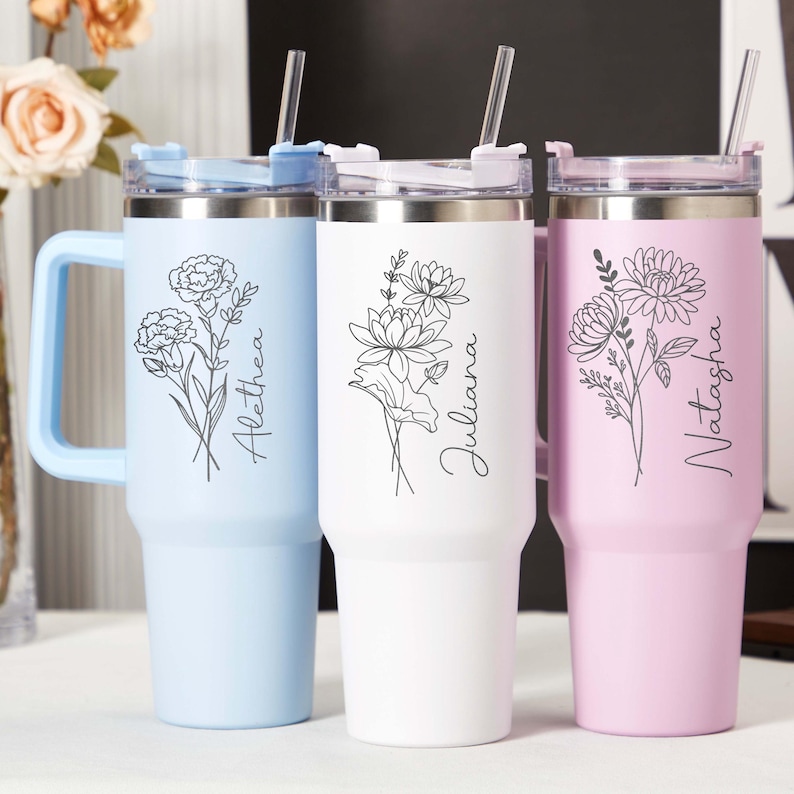 May include: Three insulated tumblers in light blue, white, and pink, each with a floral design and a name in black script. The tumblers have handles, clear lids, and straws. The names are Alethea, Juliana, and Natasha.