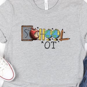 Könnte beinhalten: Ein hellgraues T-Shirt mit dem Schriftzug "SCHOOL OT" in einem farbenfrohen Design. Das Design umfasst einen Apfel, einen Globus, einen Bleistift und eine Tafel. Das Shirt wird mit blauen Jeans und weißen Turnschuhen kombiniert.