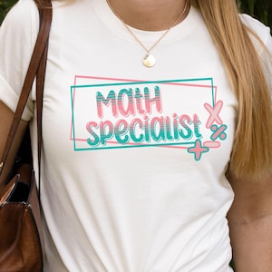 May include: A white t-shirt with the words "MATH SPECIALIST" in pink and teal, framed by a teal rectangle and decorated with math symbols. The shirt is knotted at the waist.