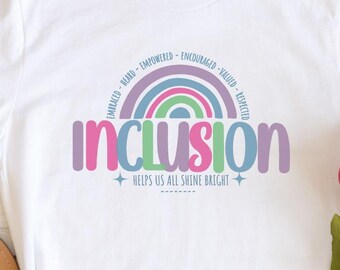 Può includere: T-shirt bianca con la parola "INCLUSION" in viola e verde, sopra il testo "HELPS US ALL SHINE BRIGHT". Un design arcobaleno si inarca sopra la parola "INCLUSION" con parole come "EMBRACED" e "VALUED". La maglietta è esposta con sandali e fiori.