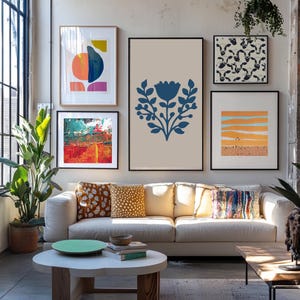 May include: A living room scene featuring a white sofa with decorative pillows and a round coffee table. Above the sofa, framed abstract art pieces in various colors and styles are displayed, creating a gallery wall aesthetic.