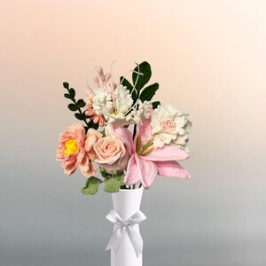 Puede incluir: Un ramo de flores de ganchillo de color rosa y blanco en un jarrón blanco con un lazo blanco.