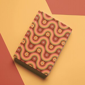 May include: A closed notebook with a retro-style design. The cover features a repeating pattern of wavy lines in shades of brown, orange, and green, interspersed with small flower motifs. The notebook is set against a backdrop of orange and red.