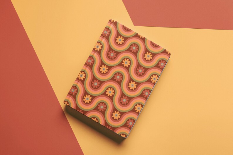 May include: A closed notebook with a retro-style design. The cover features a repeating pattern of wavy lines in shades of brown, orange, and green, interspersed with small flower motifs. The notebook is set against a backdrop of orange and red.