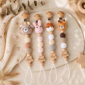 May include: Four dummy clips featuring crocheted animal heads, including a bear, rabbit, fox, and tiger. Each clip has wooden beads, a star-shaped wooden charm engraved with names Oliver, Amelia, Noah, and Emma, and a white loop attachment.