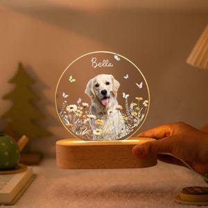 Może przedstawiać: Okrągła, podświetlana lampka nocna z psem Golden Retriever w polu kwiatów. Imię "Bella" jest napisane nad psem. Światło spoczywa na drewnianej podstawie i jest otoczone motylami.