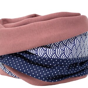 Op de afbeelding: Een roze, blauwe en witte gepatroneerde nekwarmer. De nekwarmer is gemaakt van zachte stof en heeft een omkeerbaar ontwerp.