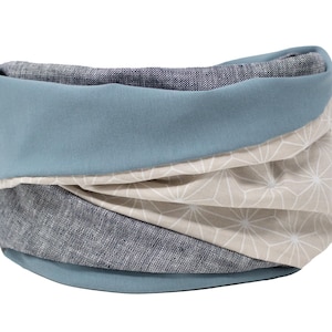 Op de afbeelding: Een blauwe, beige en grijze stoffen nekwarmer met een geometrisch patroon.