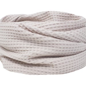 Könnte beinhalten: Ein hellbeige Waffelstrick-Cowl-Schal, gefaltet und drapiert. Der Stoff hat ein strukturiertes, gitterartiges Muster. Der Schal hat eine neutrale Farbe und ist für verschiedene Outfits geeignet. Der Artikel wird vor weißem Hintergrund präsentiert.