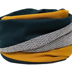 Puede incluir: Un calentador de cuello doblado con un esquema de color verde oscuro, blanco y amarillo mostaza. El calentador tiene un patrón geométrico en blanco y negro.