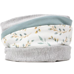 Könnte beinhalten: Ein grauer und blauer Stoff-Halswärmer mit einem weißen Blumenmuster. Das Blumenmuster zeigt kleine grüne und gelbe Blätter.