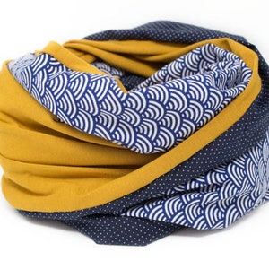 Op de afbeelding: Een oneindige sjaal in mosterdgeel en marineblauw met een wit en blauw golfpatroon aan de ene kant en een marineblauwe kant met witte stippen.