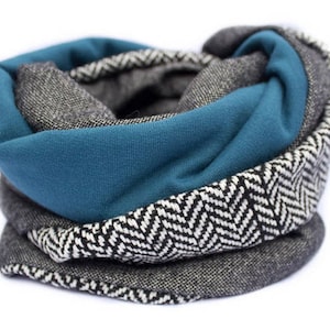 Puede incluir: Una bufanda infinita de patrón gris y negro con una capa de tela azul turquesa.