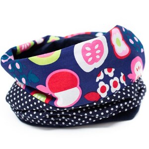 Op de afbeelding: Een marineblauwe nekwarmer met een kleurrijk fruitprint aan de ene kant en een wit stippenpatroon aan de andere kant.