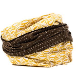 May include: A brown and yellow fabric neck warmer with a geometric pattern. The fabric is folded over and the pattern is visible on both sides.