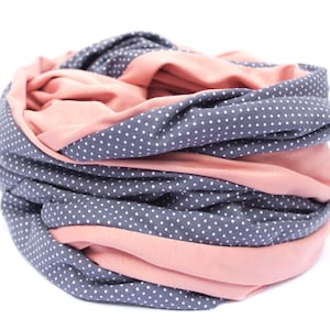 May include: A soft, cozy scarf with a reversible design. One side is a solid pink color, while the other side features a gray background with white polka dots.