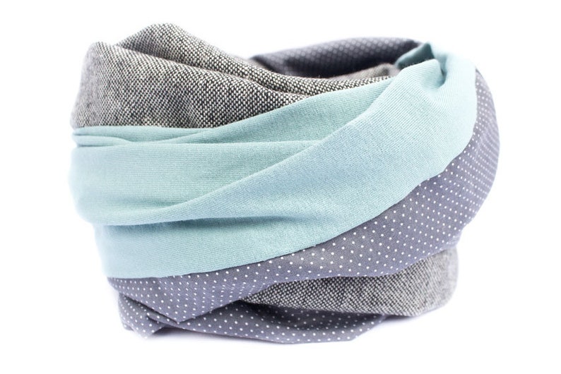 K&ouml;nnte beinhalten: Ein grauer, blauer und wei&szlig;er gemusterter Infinity-Schal. Der Schal ist aus weichem Stoff und perfekt, um sich im Winter warm zu halten.