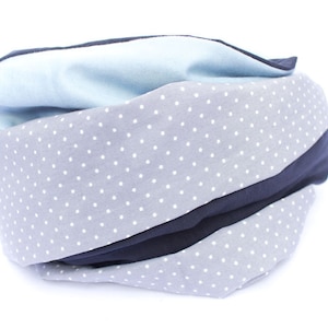May include: A gray and blue fabric neck warmer with white polka dots. The neck warmer is folded and rolled up.