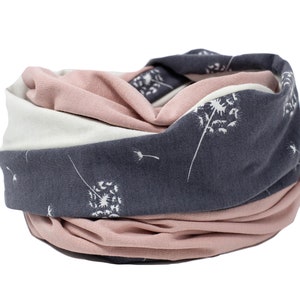 May include: A soft, stretchy neck warmer with a white dandelion print on a grey background. The neck warmer is folded in half and has a pink layer on the inside.