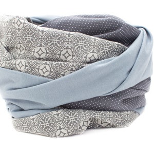 May include: A soft, blue and gray patterned scarf with a geometric design. The scarf is folded and rolled into a circular shape.