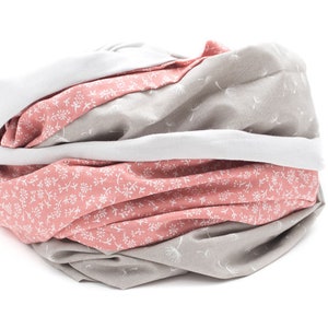 May include: A soft, cozy neck warmer made of two different fabrics. One side is a light gray with a subtle white floral pattern, while the other side is a pink fabric with a white floral pattern.