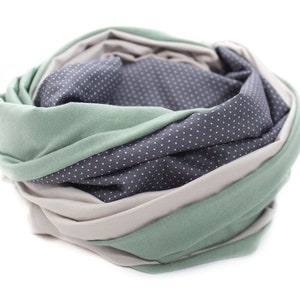 May include: A soft, multi-colored scarf with a green, beige, and gray polka dot pattern. The scarf is folded and rolled into a circle.