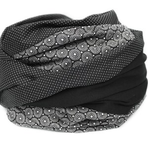 May include: Black and white patterned fabric scarf with a black solid fabric section. The scarf is folded and rolled into a circular shape.