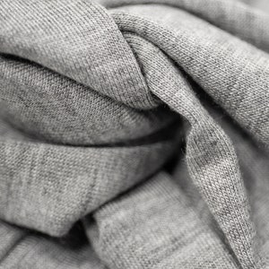 May include: Close-up of a gray fabric with a textured surface. The fabric is folded and twisted, creating a soft and inviting look.