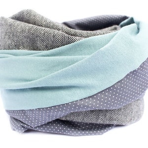May include: A gray, blue, and white patterned infinity scarf. The scarf is made of soft fabric and is perfect for keeping warm in the winter.