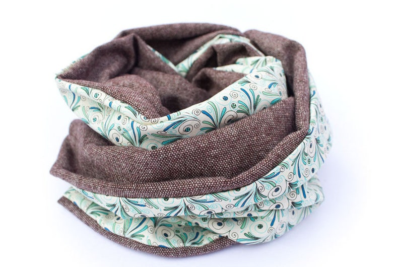 Peut inclure: Une &eacute;charpe infinie marron et blanche avec un motif floral. L'&eacute;charpe est faite d'un tissu doux et textur&eacute;.