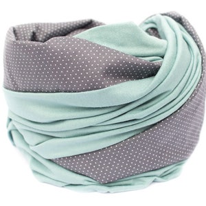 May include: A soft, gray and teal scarf with a white polka dot pattern. The scarf is folded and twisted, creating a unique and stylish look.
