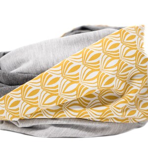 May include: A gray and yellow reversible infinity scarf with a geometric pattern. The scarf is made of soft, comfortable fabric and is perfect for adding a touch of style to any outfit.