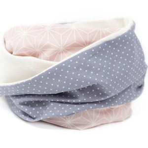 May include: A reversible neck warmer with a pink geometric pattern on one side and a gray fabric with white polka dots on the other side.