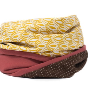 May include: A brown, red, and yellow patterned neck warmer. The neck warmer is made of fabric and has a geometric pattern.