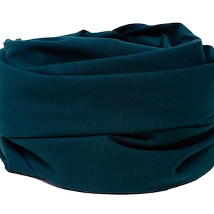 Op de afbeelding: Een teal blauwe nekwarmer van stof, gevouwen en gerold in een buisvorm.