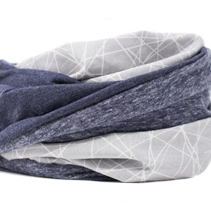 May include: A rolled neck warmer in shades of gray and navy blue. The neck warmer is made of soft fabric and features a geometric pattern in white on a gray background. The design is a mix of solid and patterned sections.