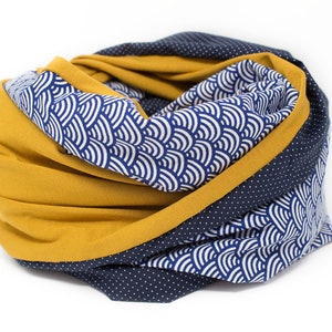 May include: A reversible infinity scarf with a mustard yellow side and a navy blue side. The navy blue side has a white wave pattern and white polka dots.