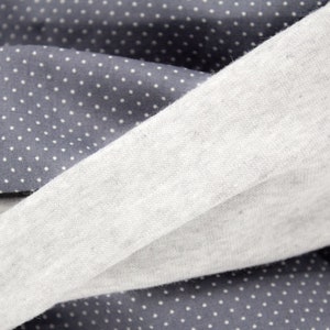 Puede incluir: Primer plano de dos telas, una gris con lunares blancos y la otra gris claro liso. Las telas est&aacute;n dobladas una sobre la otra, creando un aspecto texturizado.