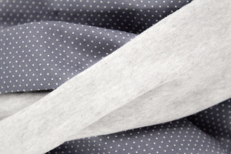 Puede incluir: Primer plano de dos telas, una gris con lunares blancos y la otra gris claro liso. Las telas est&aacute;n dobladas una sobre la otra, creando un aspecto texturizado.