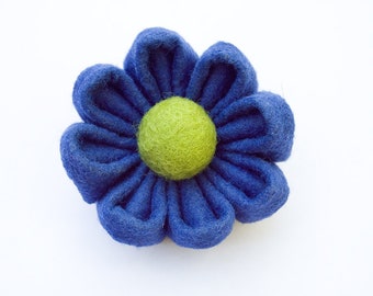 Könnte beinhalten: Eine blaue Filzblume mit einem grünen Filzmittelpunkt. Die Blume ist handgefertigt und hat ein schlichtes, elegantes Design.