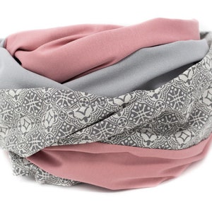 May include: A gray and pink patterned infinity scarf with a geometric design. The scarf is made of soft fabric and is perfect for adding a touch of style to any outfit.