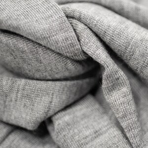 May include: Close-up of a gray fabric with a textured surface. The fabric is folded and twisted, creating a variety of folds and creases.