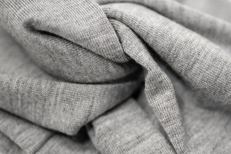 May include: Close-up of a gray fabric with a textured surface. The fabric is folded and twisted, creating a variety of folds and creases.