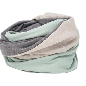 May include: A soft, cozy neck warmer made of three different fabrics. The neck warmer is gray, beige, and light green. The beige fabric has a subtle white pattern.