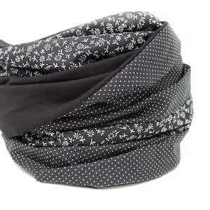 May include: A black and white patterned infinity scarf with a black solid fabric section. The scarf is folded and rolled into a circular shape.