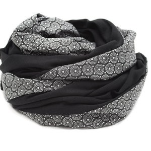 May include: Black and white patterned infinity scarf. The scarf is made of a soft, stretchy fabric and is perfect for adding a touch of style to any outfit.