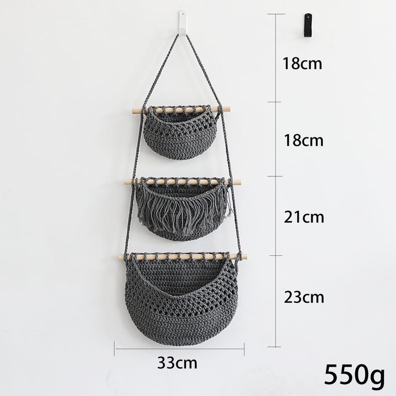 Puede incluir: Un colgante de pared de macram&eacute; gris con tres cestas tejidas. Las cestas est&aacute;n unidas a tacos de madera y suspendidas por una cuerda gris. La cesta inferior mide 33 cm de ancho y 23 cm de alto. El peso total es de 550 g.