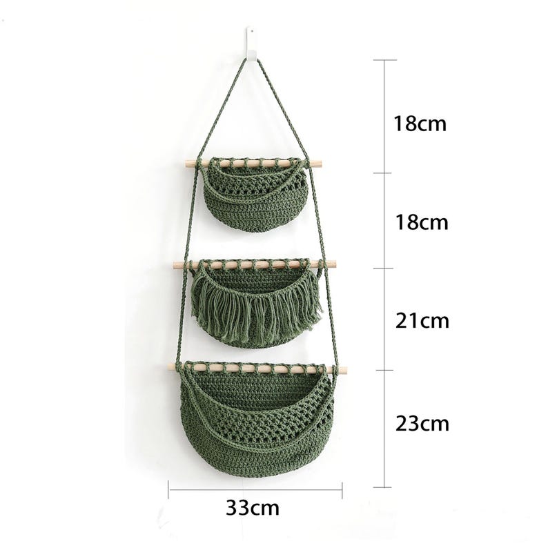Puede incluir: Un colgador de plantas de macram&eacute; de tres niveles en verde oliva. Cada nivel es una cesta tejida suspendida por una cuerda y una clavija de madera. La cesta inferior mide 33 cm de ancho y 23 cm de alto. Las dos cestas superiores miden 18 cm de alto. La cesta del medio tiene flecos.