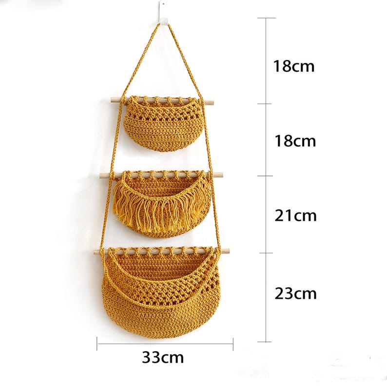 Puede incluir: Cestas de almacenamiento colgantes de tres niveles de color amarillo mostaza. Las dos cestas superiores miden 18 cm de alto, la cesta central tiene flecos y mide 21 cm de alto, y la cesta inferior mide 23 cm de alto y 33 cm de ancho. Cada cesta est&aacute; suspendida por una cuerda natural.