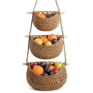 Może przedstawiać: Trzypoziomowy wiszący kosz na owoce wykonany z plecionego brązowego materiału. Każdy kosz wypełniony jest różnymi owocami, w tym pomarańczami, śliwkami i jabłkami. Kosze zawieszone są na sznurach i drewnianych kołkach, rustykalne rozwiązanie.